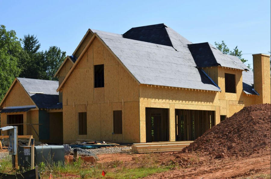 An under-construction house with a pile of dirt in the foreground. The house only has the plywood and roof wrap.